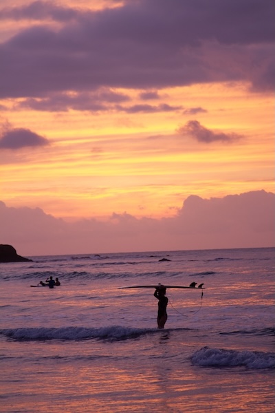 Frau hält Surfbrett über Kopf im Wasser bei Sonnenuntergang