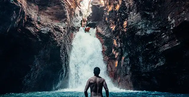 Ein Mann steht im Wasser vor einem Wasserfall.