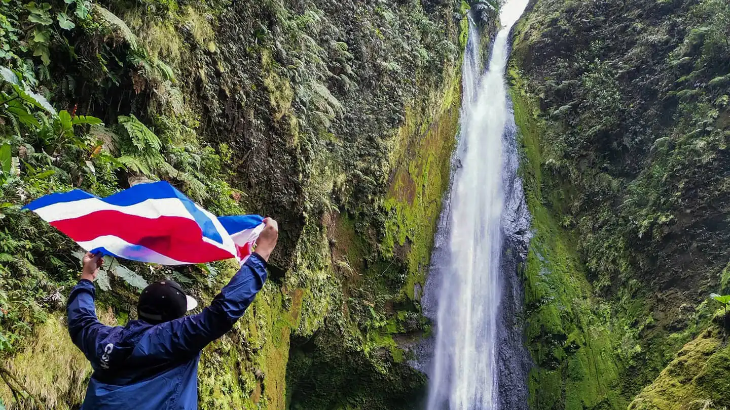 Ein Mann hält eine Fahne vor einem Wasserfall.