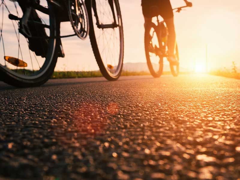 Eine Person fährt bei Sonnenuntergang mit dem Fahrrad eine Straße entlang.