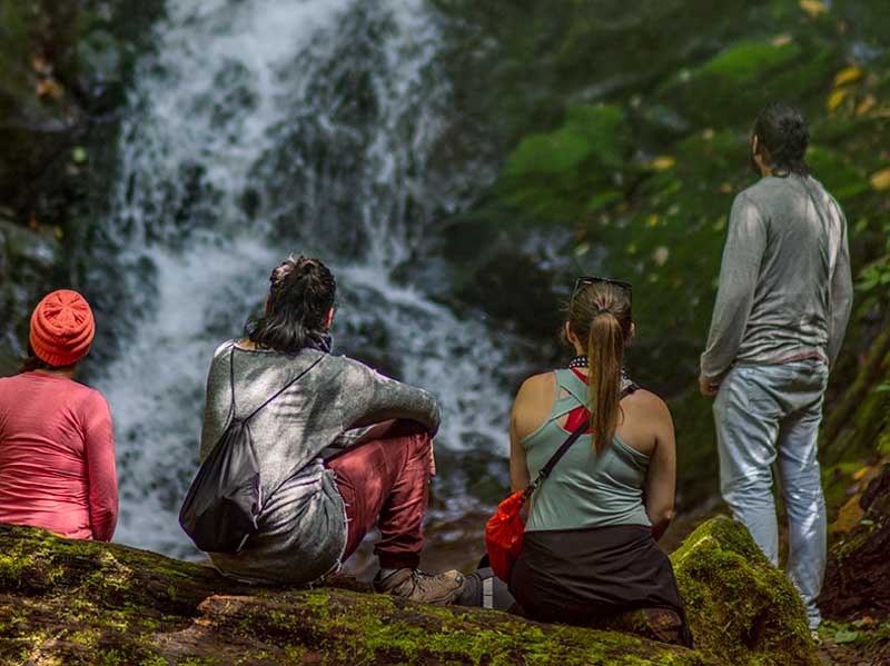 Eine Gruppe von Menschen sitzt auf einem Felsen und schaut auf einen Wasserfall.