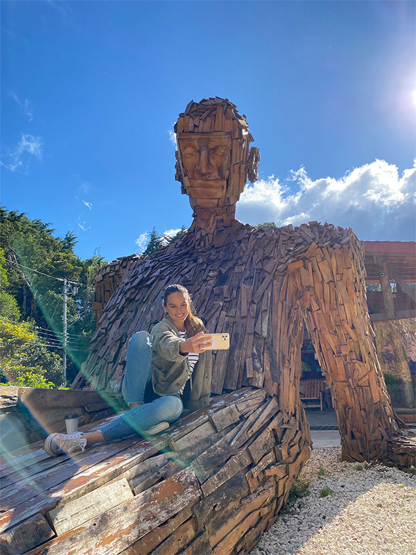 Eine Frau sitzt auf einer Holzskulptur.