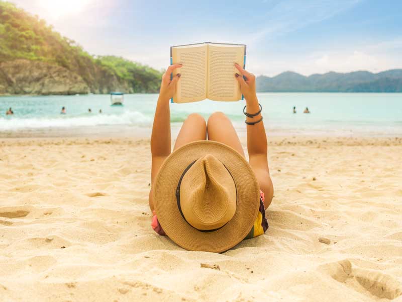 Eine Frau liegt am Strand und liest ein Buch.
