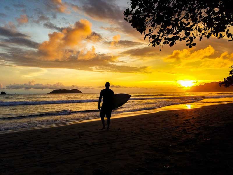 Ein Mann hält ein Surfbrett in der Hand und steht am Strand.