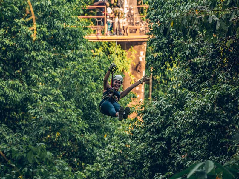 Eine Frau auf einer Seilrutsche mitten im Wald.