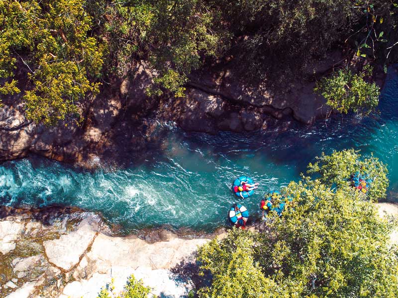 Eine Gruppe von Menschen in Flößen paddelt einen Fluss hinunter.