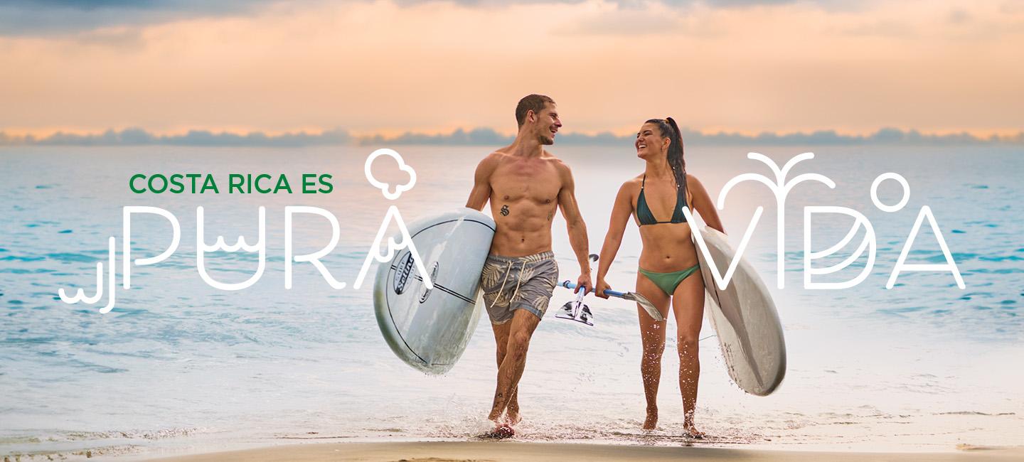 Paar, das am Strand spazieren geht, mit Surfbrettern undpura vida"-Text um sie herum