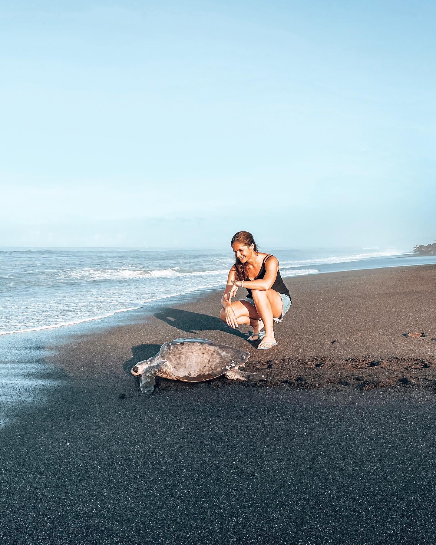 Eine Frau steht neben einer Schildkröte am Strand