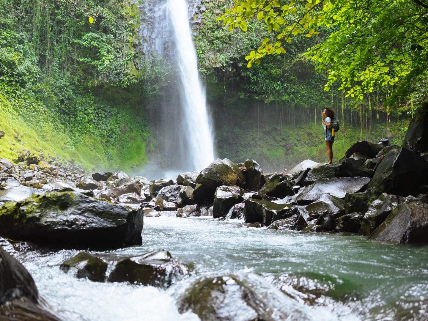 Frau steht neben einem Wasserfall im Dschungel