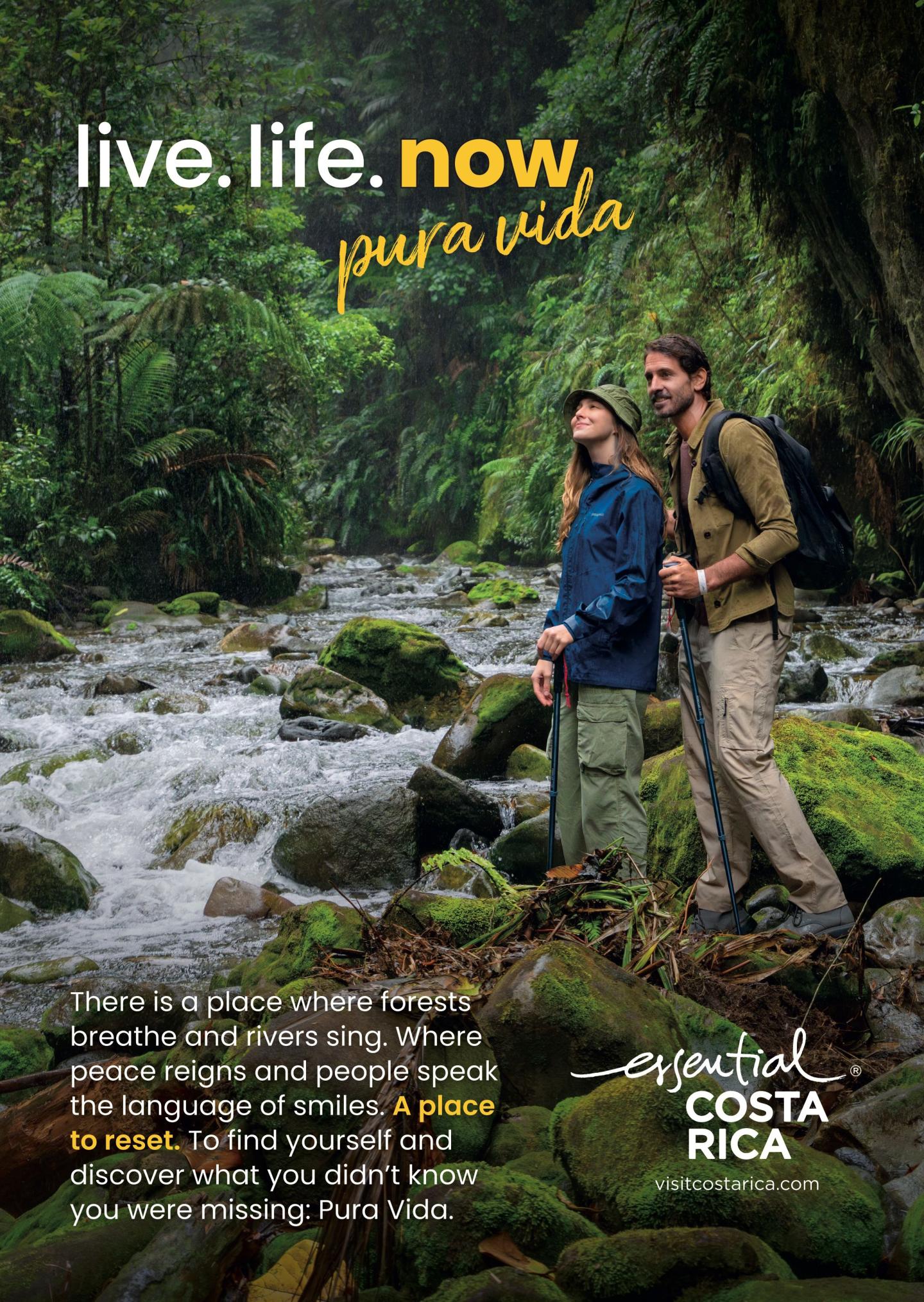 Anzeige, die zwei Wanderer zeigt, die auf moosbewachsenen Felsen neben einem Fluss in einem üppigen Regenwald stehen. Überschrift: „live.life.now“ undpura vida“. Der Text beschreibt Wälder, die atmen, Flüsse, die singen, und die Möglichkeit, neu durchzustarten. Logo: „esencial Costa Rica, visitcostarica.com.
