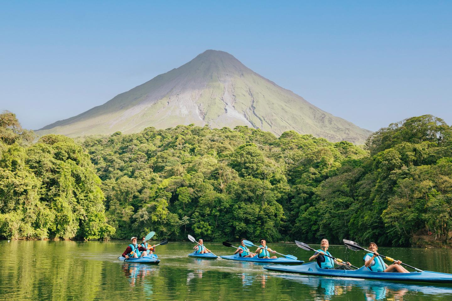 Gruppen-Kajakfahren auf einem ruhigen See, der von Regenwald gesäumt ist, mit dem Vulkan Arenal im Hintergrund.