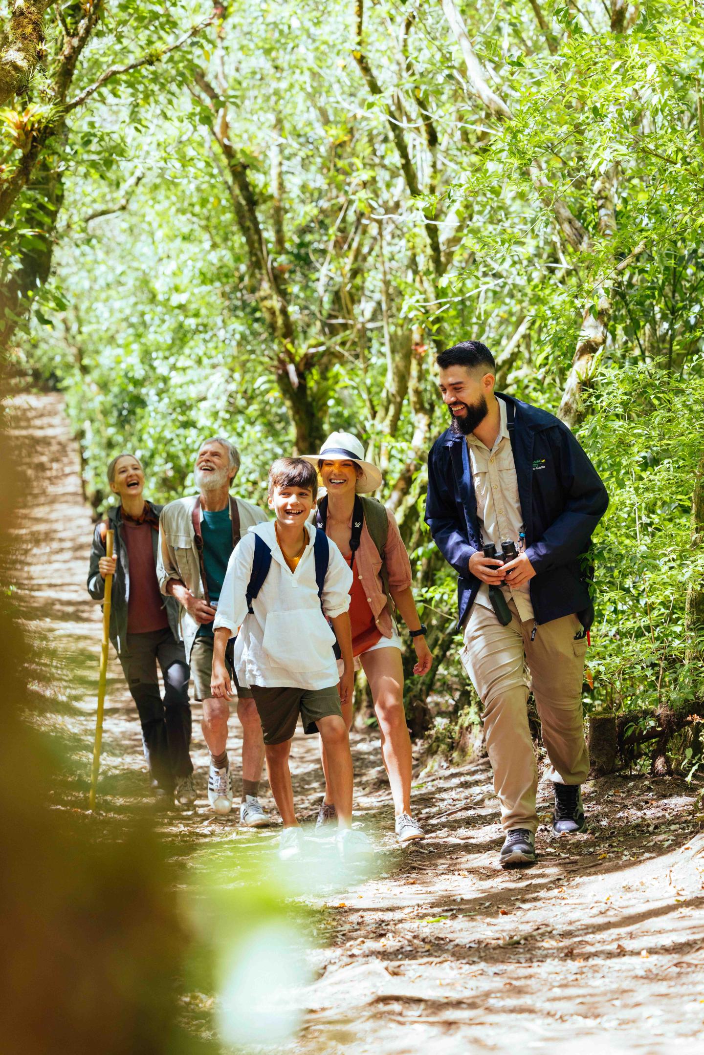 Eine kleine Gruppe von Reisenden wandert mit einem Reiseleiter auf einem schattigen Waldweg.